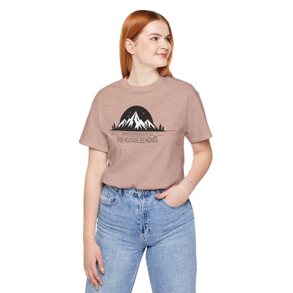 Person wearing a peach t-shirt with a mountain graphic and text, standing against a white background